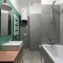Green and gray tiled walls in contemporary bathroom with white sink and bathtub in minimal style